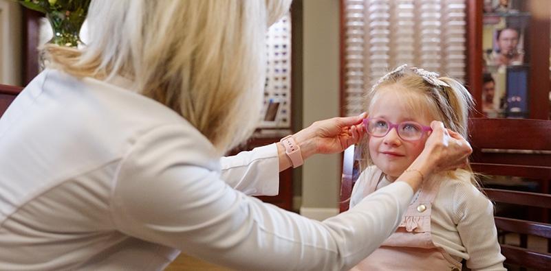 A person putting on a child's glasses

Description automatically generated